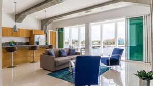 A modern living room with a sofa, blue chairs, and a kitchen area with wooden cabinets and a refrigerator. - Blue Marlin - Famous Handelskade Apartment (Willemstad)