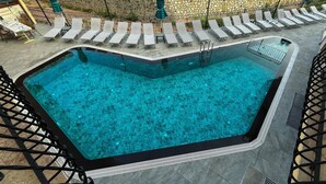 Uma piscina retangular com um deck revestido ao redor, equipada com várias espreguiçadeiras e uma pequena mesa.