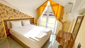 Quarto com cama grande, cabeceira de madeira, mesa de cabeceira com abajur e janela com cortinas amarelas.
