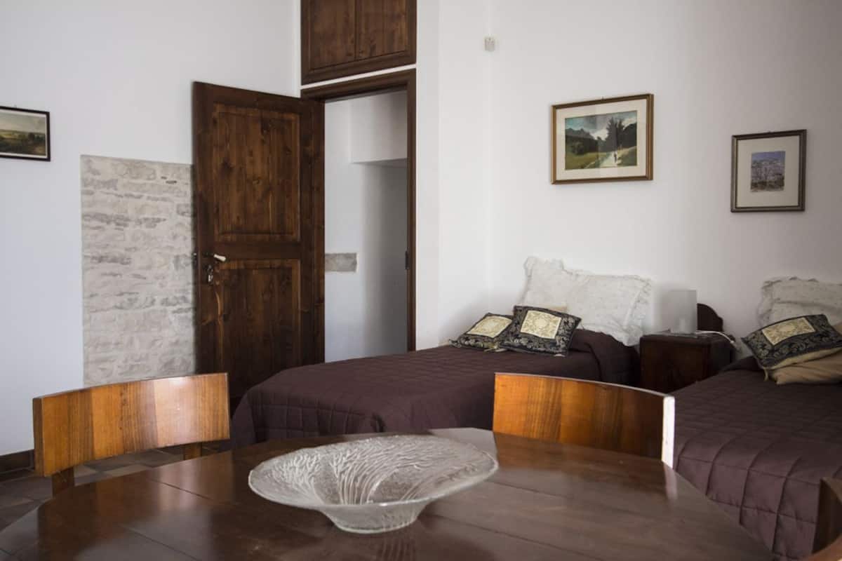Ein Zimmer mit zwei Betten, einem Holztisch und einem großen Fenster.