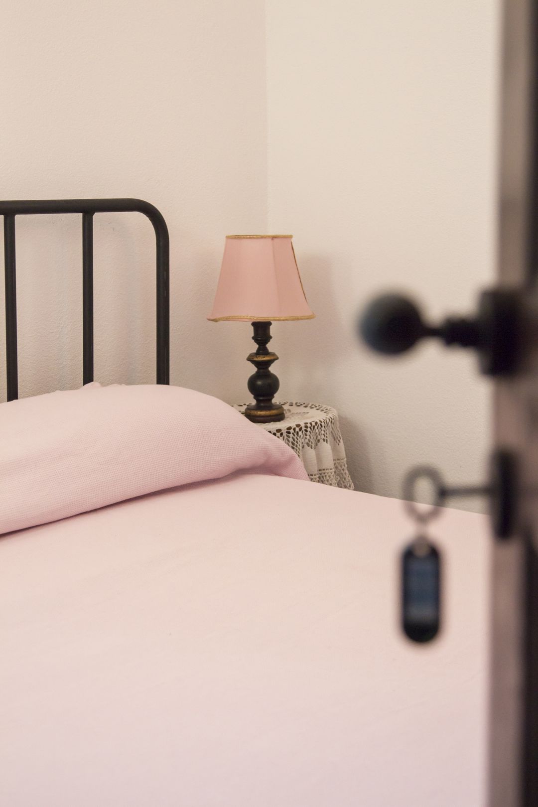 A bedroom with a bed, a bedside table with a lamp, and a door with a key lock.