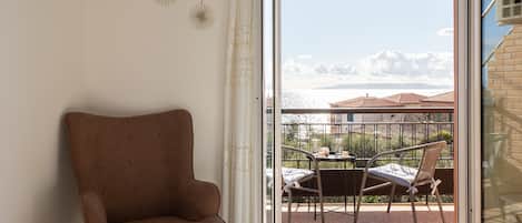 A room with a brown chair, a glass door leading to a balcony with a table and chairs, and decorative wall sconces.