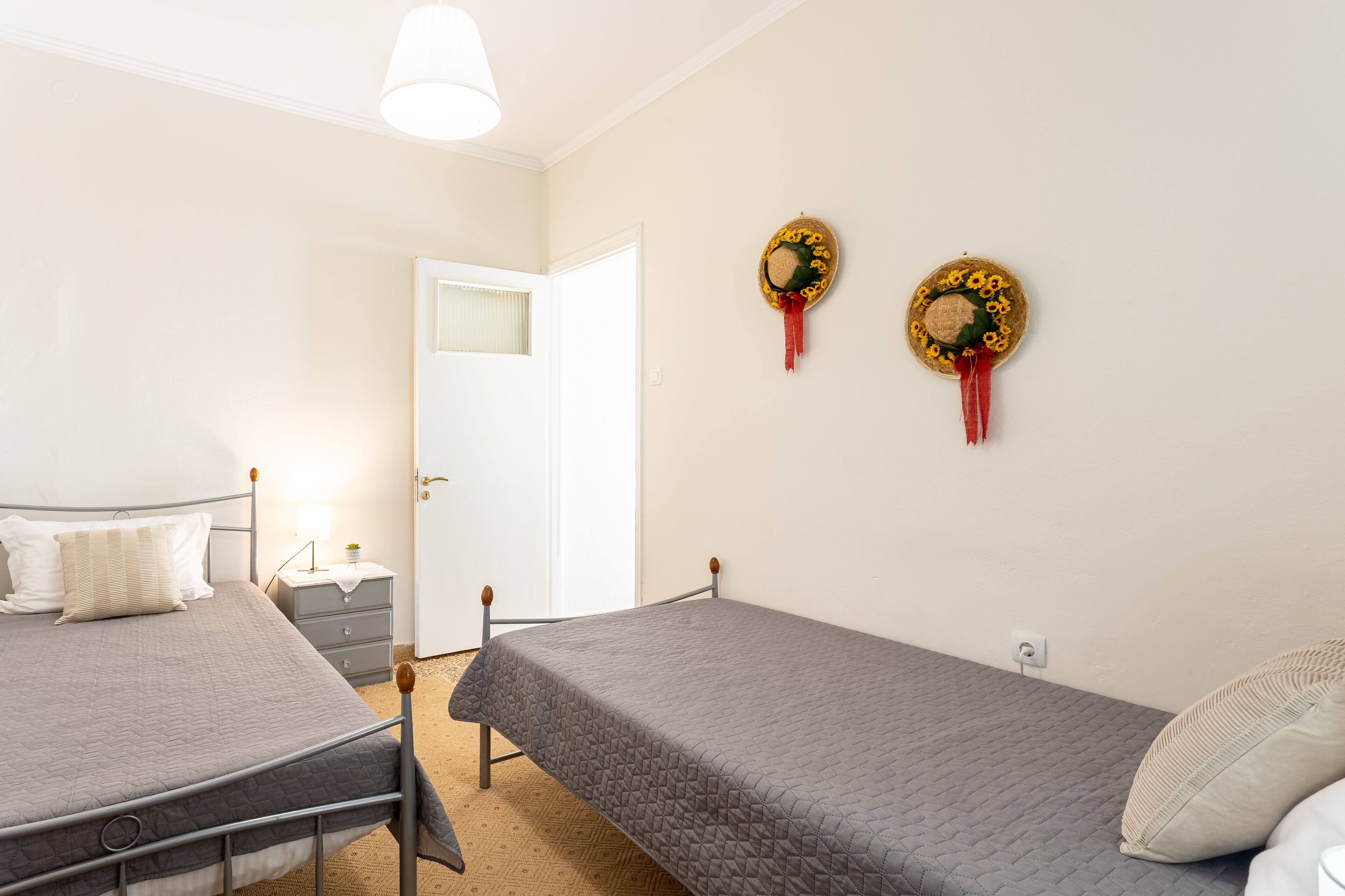 A bedroom with two single beds, a bedside table with a lamp, and a door leading to another room.