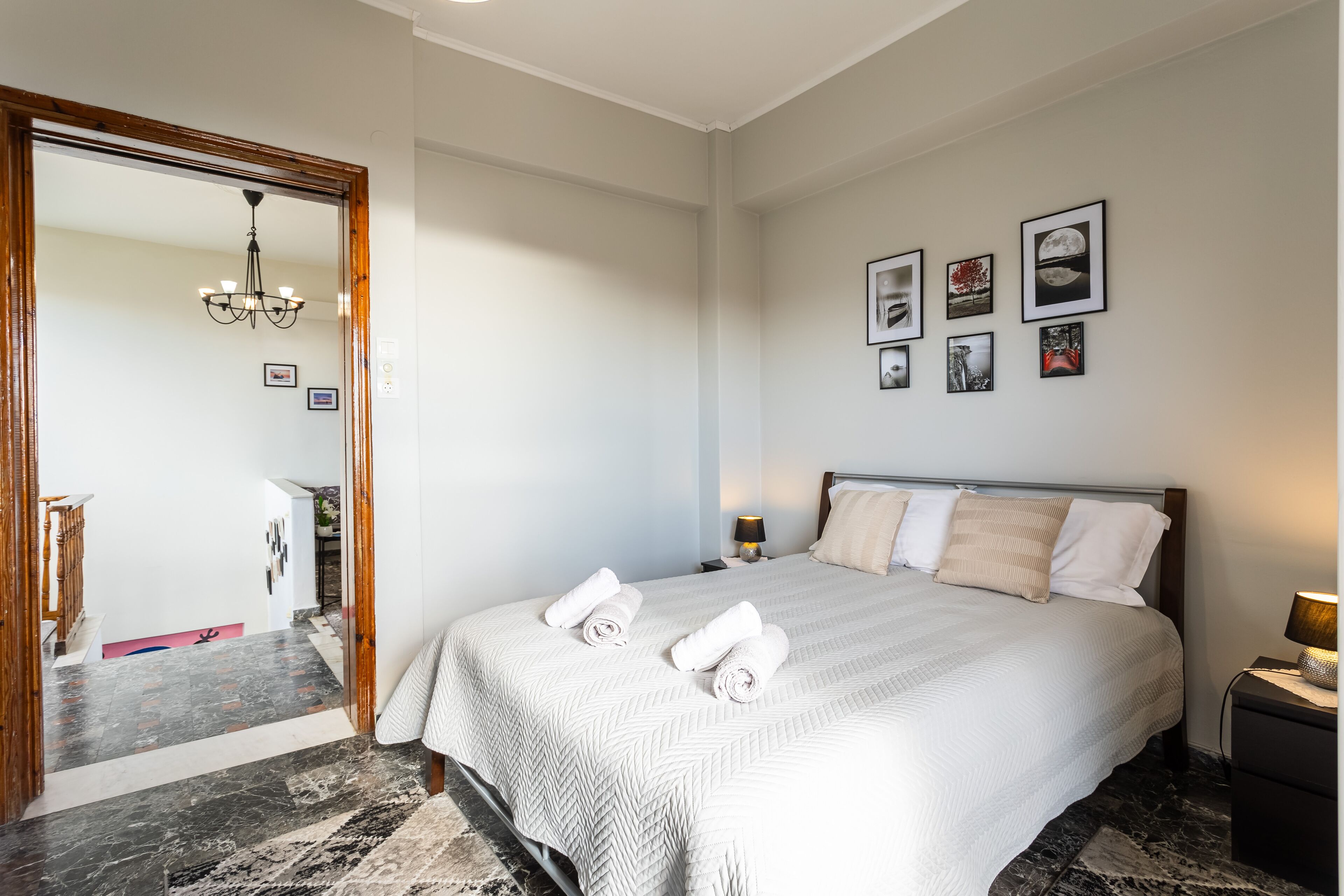A hotel room with a large bed, a wooden door, a chandelier, and framed pictures on the wall.