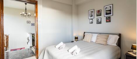 A hotel room with a large bed, a wooden door, a chandelier, and framed pictures on the wall.