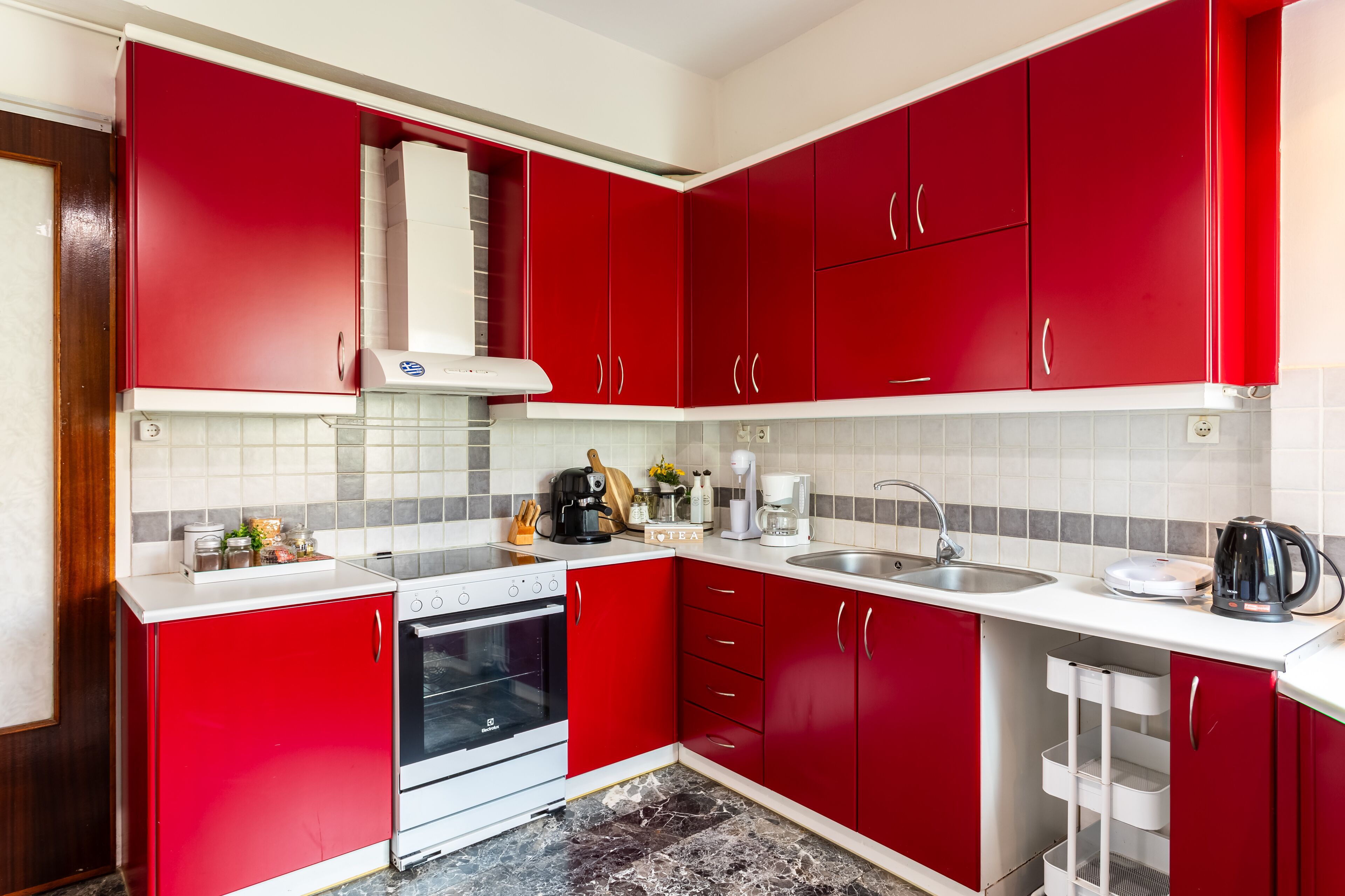 A kitchen with red cabinets, a white countertop, a stove, an oven, a sink, and a coffee maker.