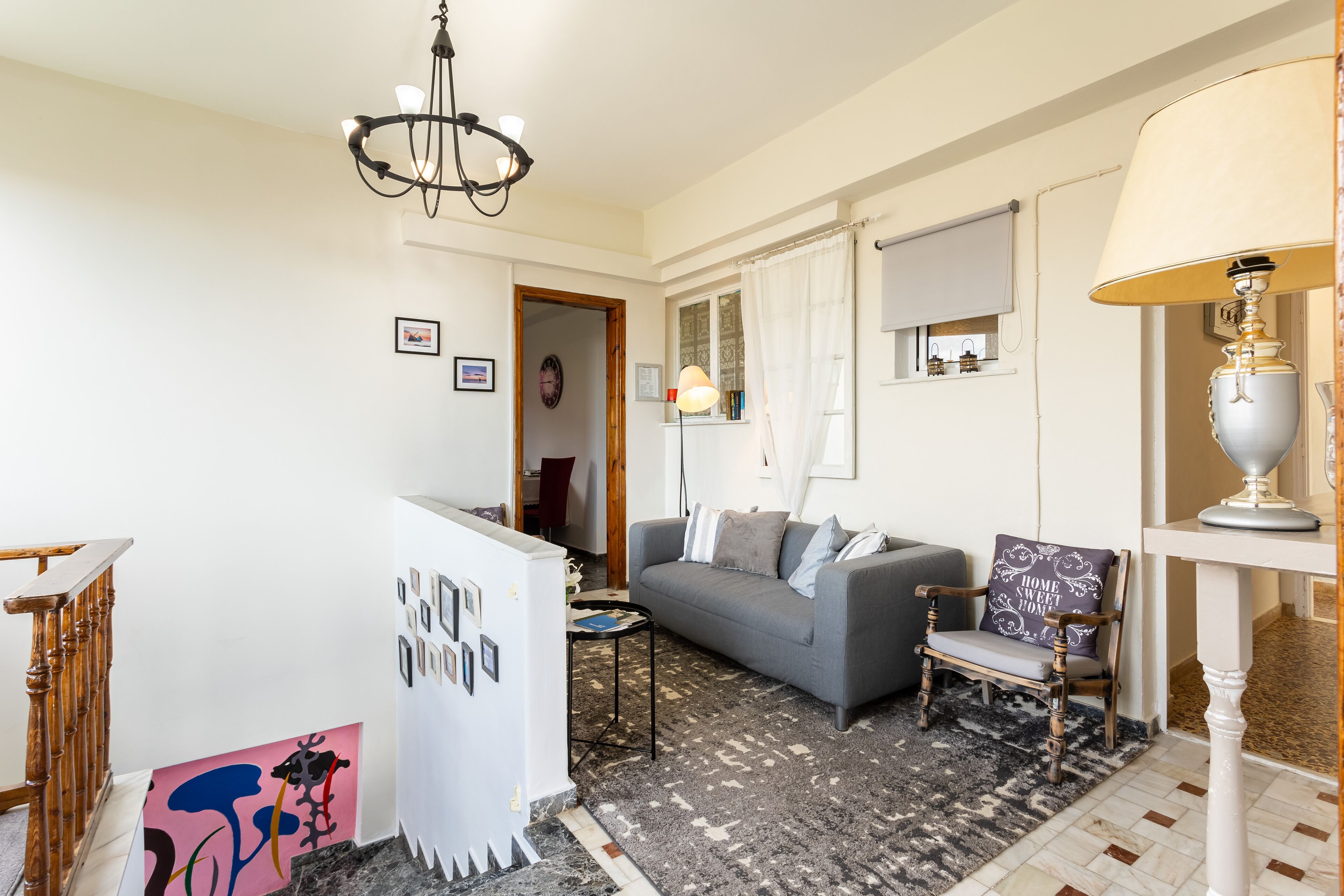 A living room with a grey sofa, a wooden chair, a small table, and a chandelier.