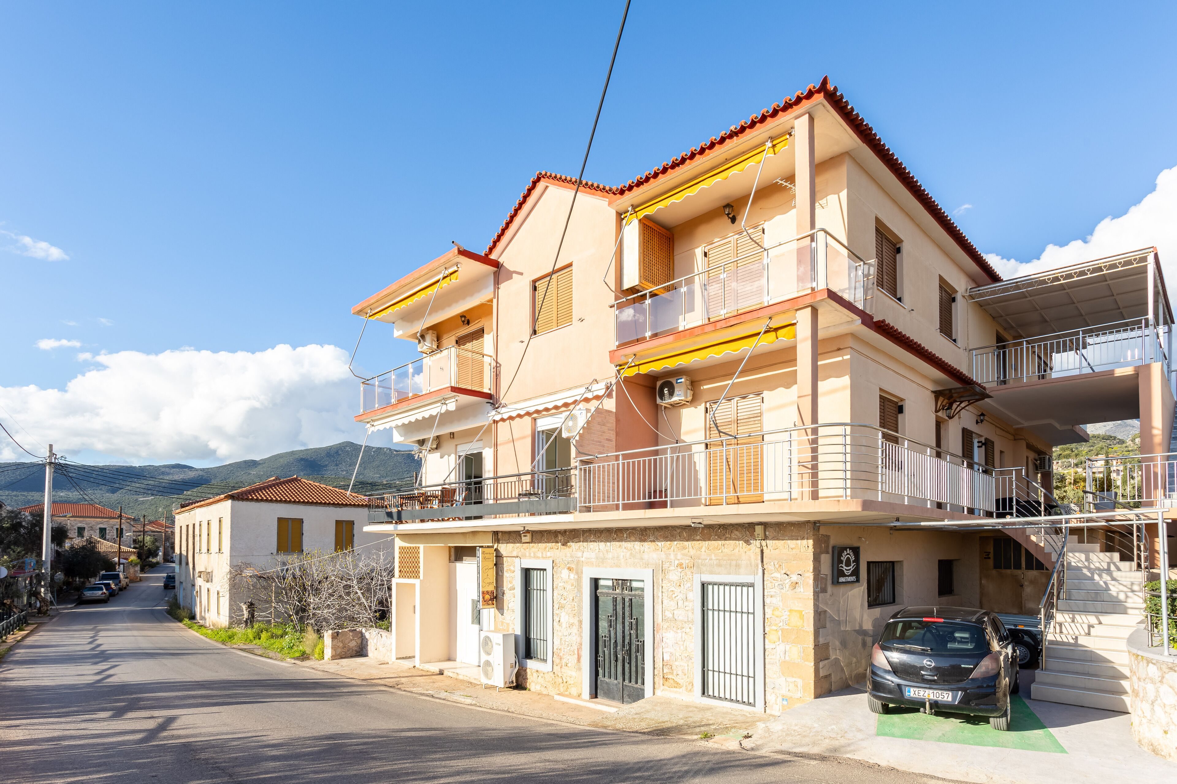 A multi-story building with balconies, a car parked in front, and a clear sky.