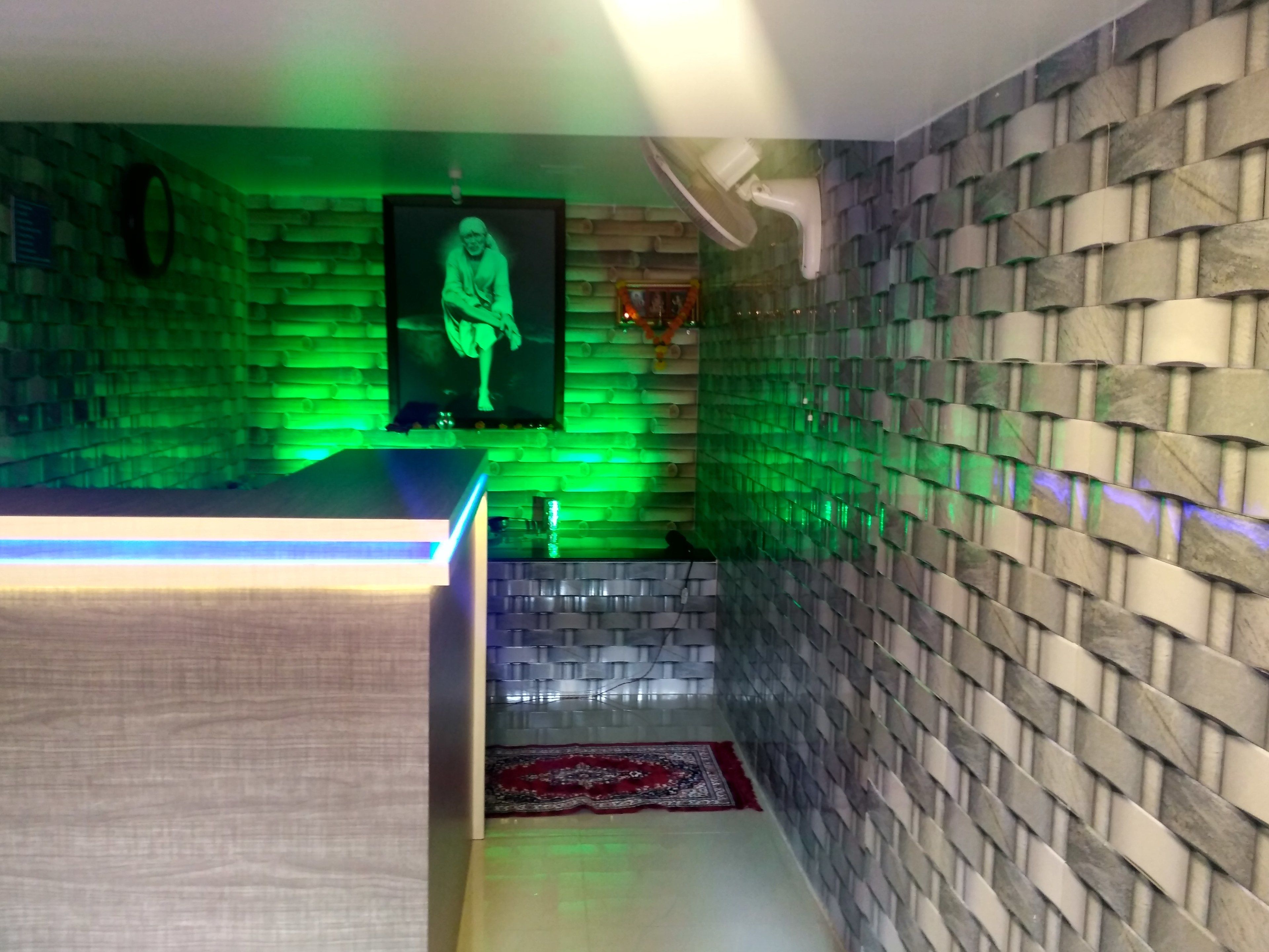 A room with a green-lit wall, a wooden reception desk, a patterned rug, and a stone-textured wall.