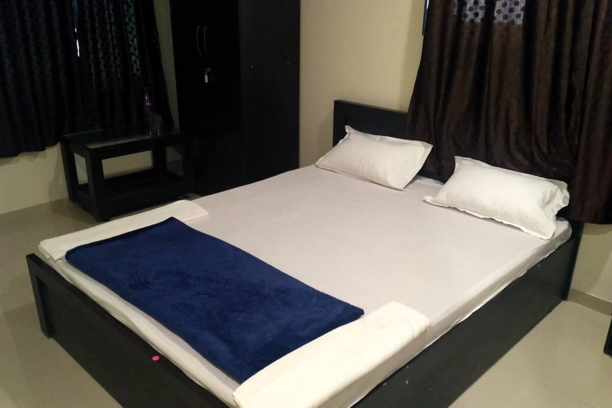 Una cama con ropa blanca, una manta azul y dos almohadas.