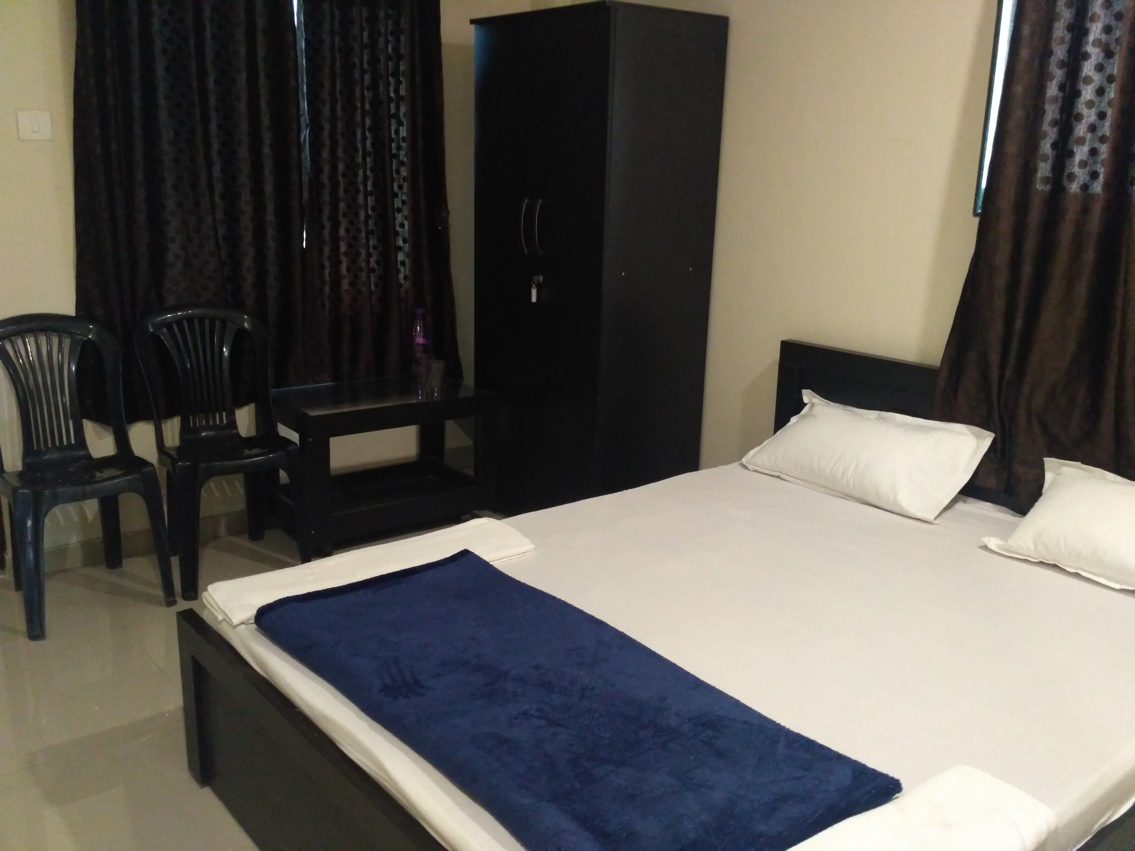 A bedroom with a bed, two chairs, a wardrobe, and a desk.
