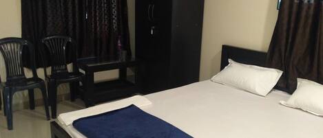 A bedroom with a bed, two chairs, a wardrobe, and a desk.