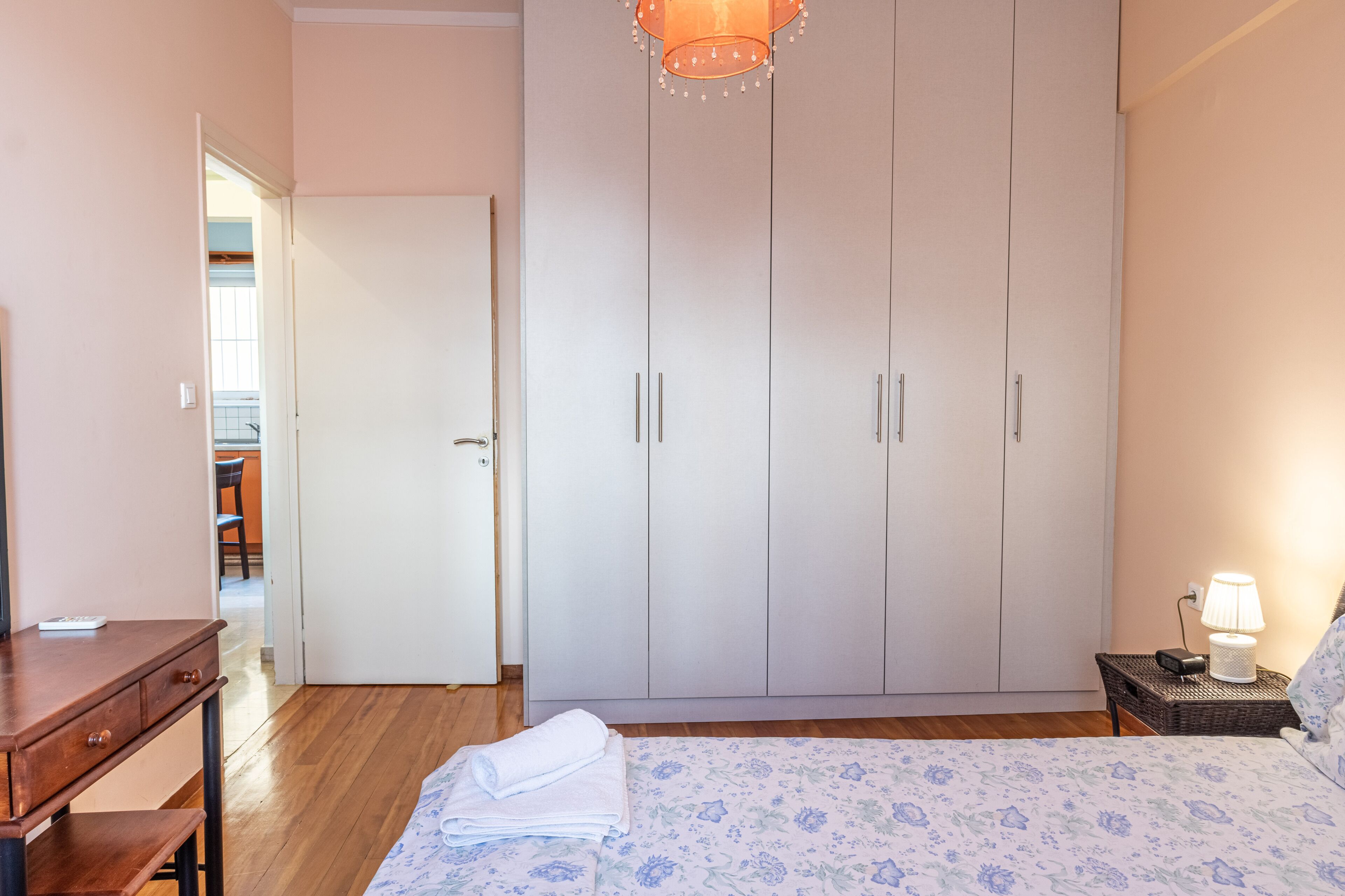 A bedroom with a bed, a desk, a wardrobe, and a nightstand with a lamp.