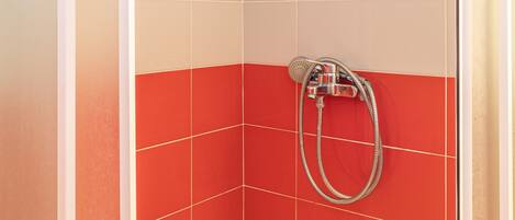 Una ducha con pared de baldosas rojas, una bañera blanca y un cabezal de ducha.