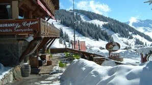 Área externa coberta de neve com um edifício de madeira, um letreiro de restaurante e um sinal de pizza.