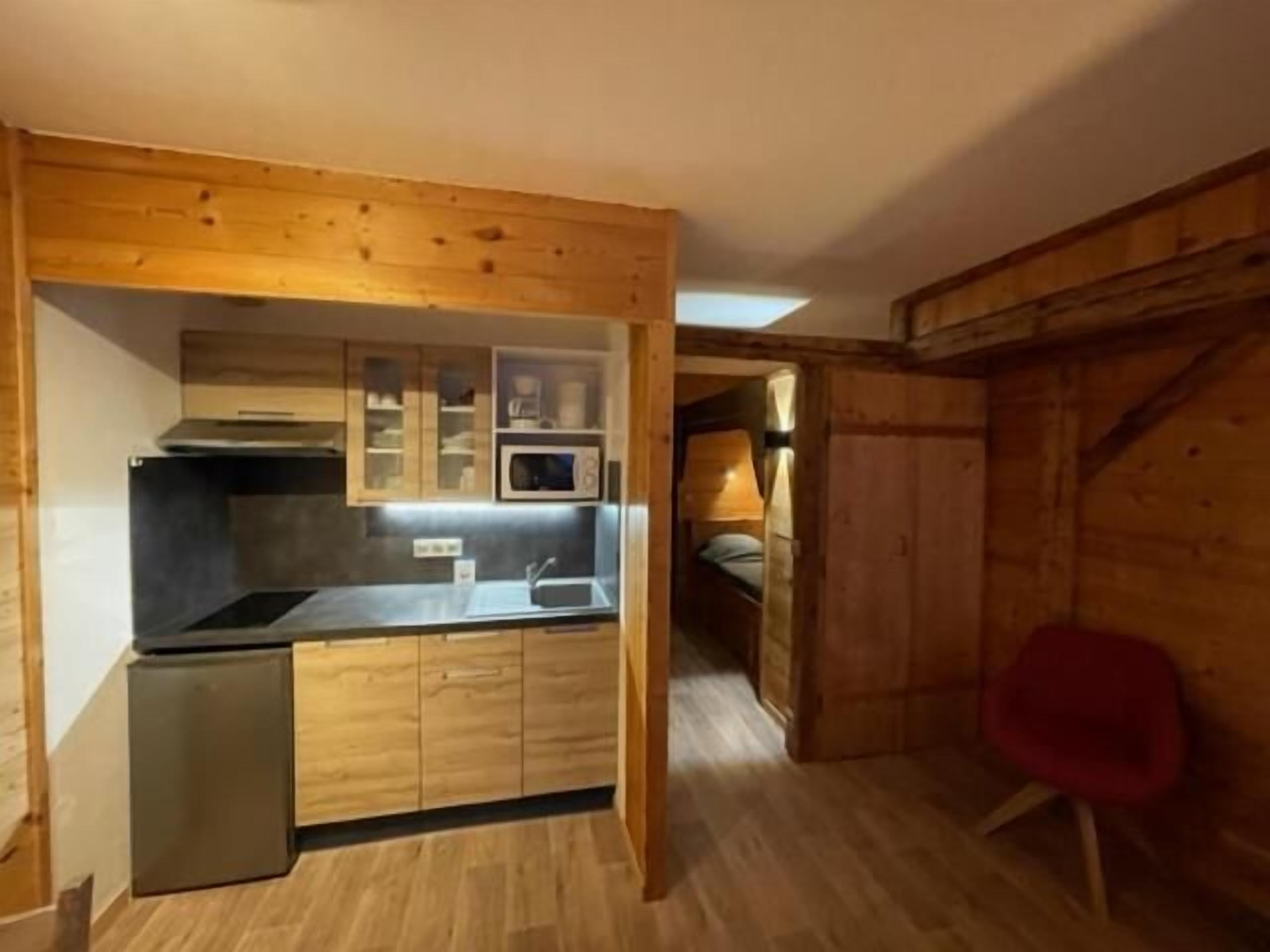 Une cuisine compacte dotée d’appareils électroménagers intégrés, de meubles de rangement en bois et d’un petit réfrigérateur.