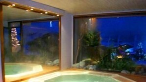 Uma banheira de hidromassagem em deck de madeira, com vista para um jardim e um prédio ao fundo.