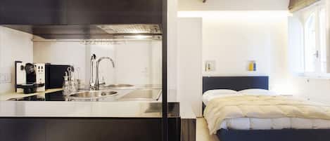 Una cocina moderna con electrodomésticos de acero inoxidable y un dormitorio independiente con cama y mesita de noche.