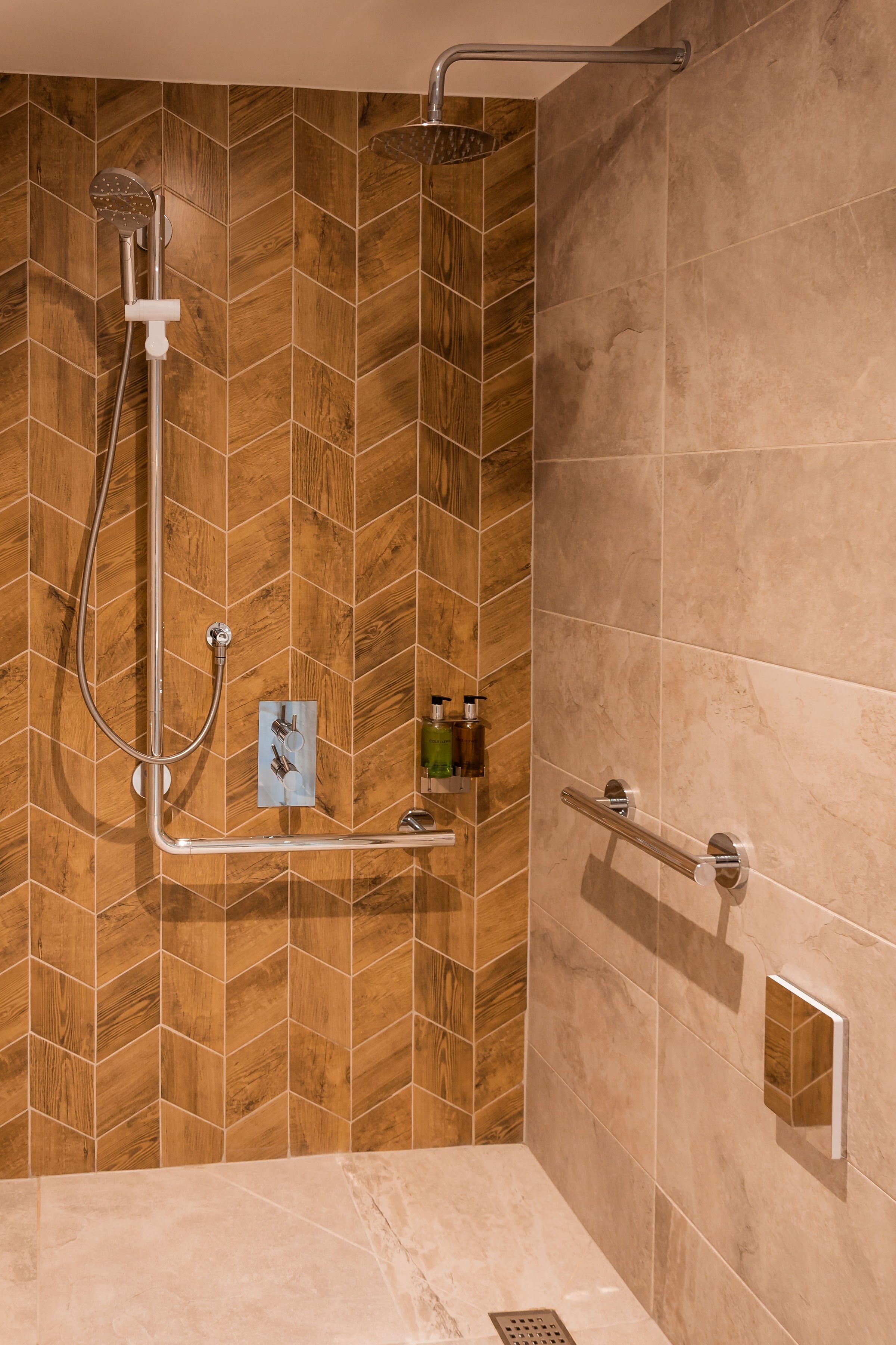 Eine moderne Dusche mit Rückwand aus Holz-Fischgrätparkett, einer Handbrause und einem Duschhandstück.