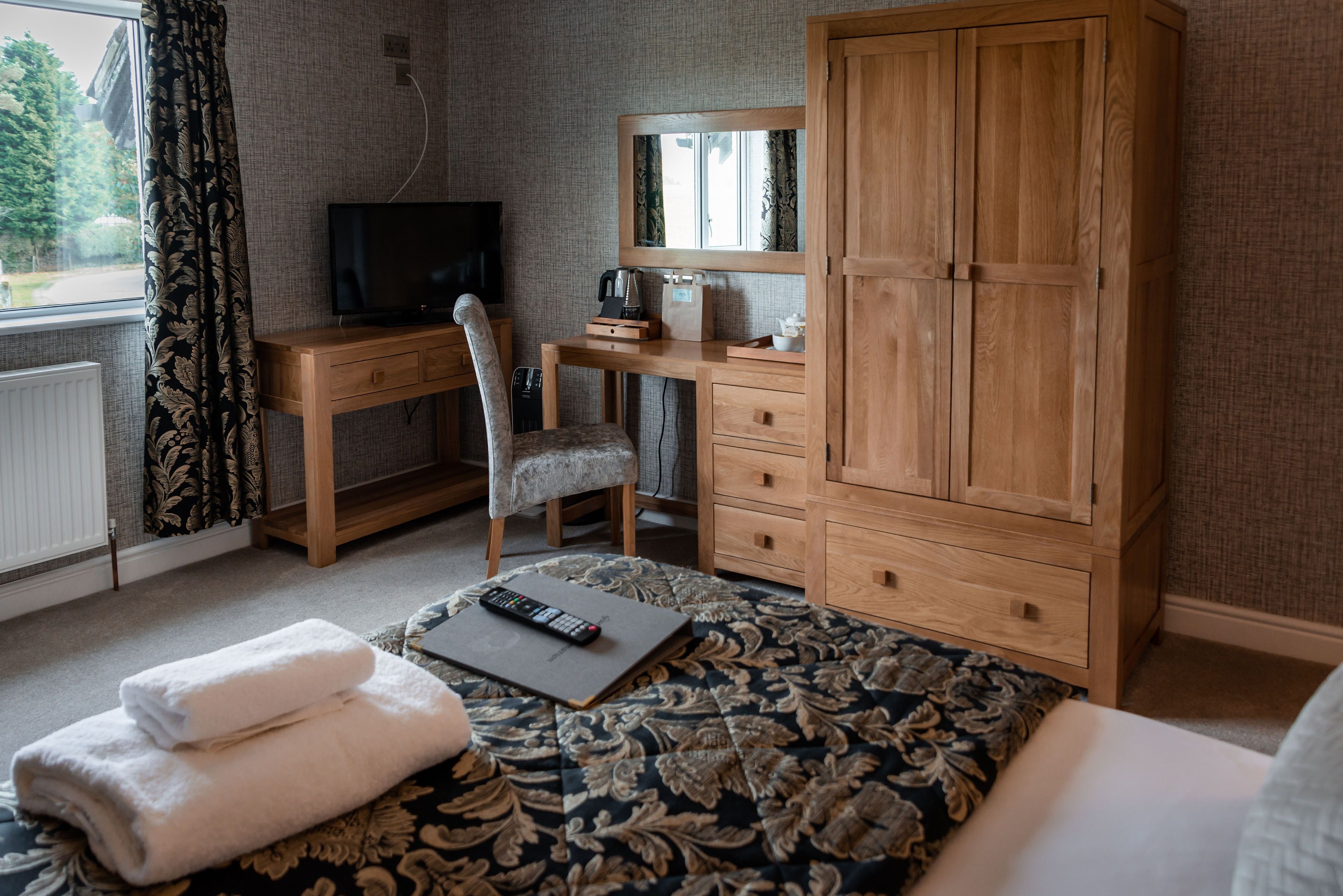 Un dormitorio con cama, escritorio con televisor, silla, armario y ventana con cortinas.