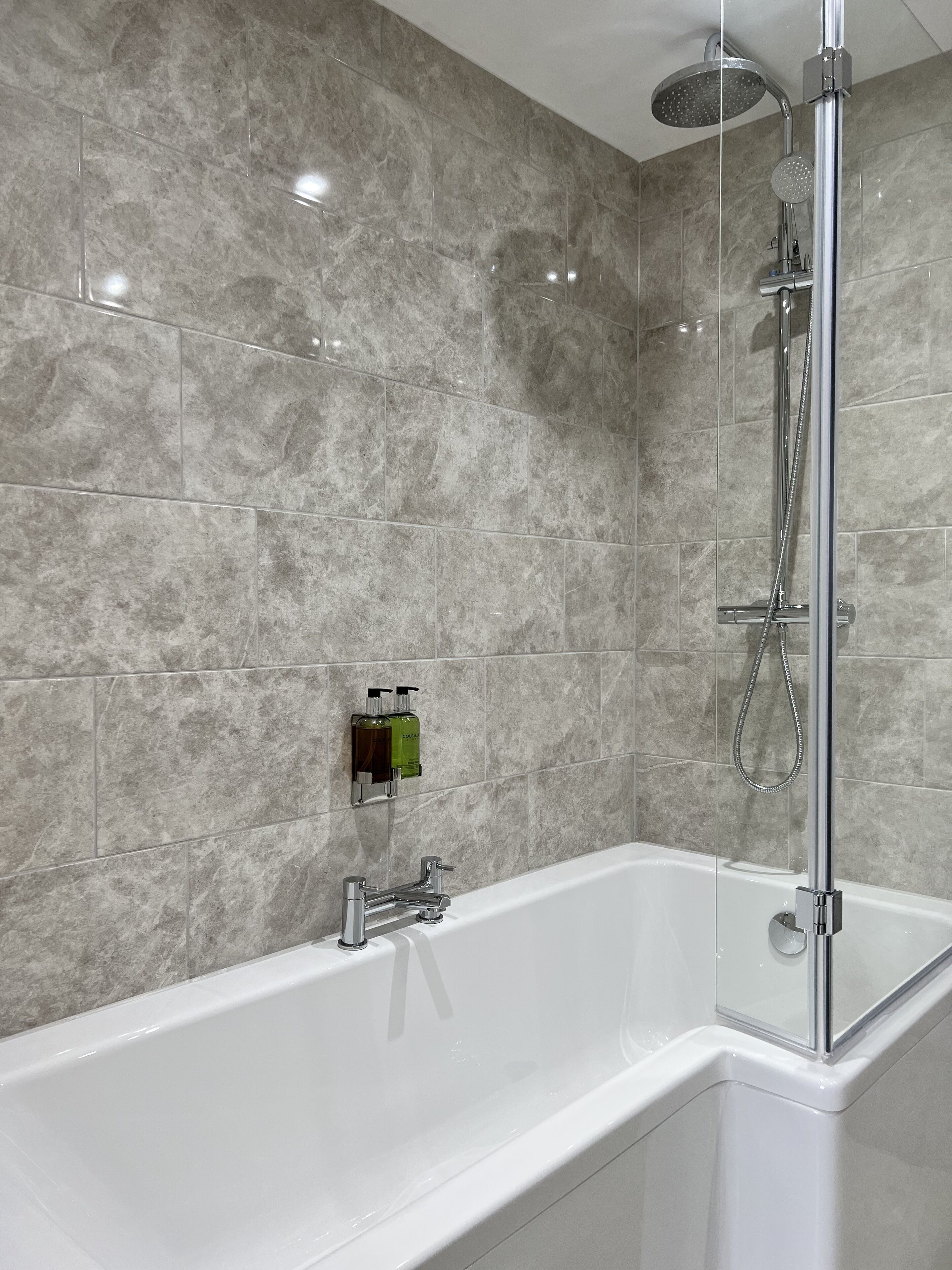 A modern bathroom with a white bathtub, a glass-enclosed shower, and marble walls.