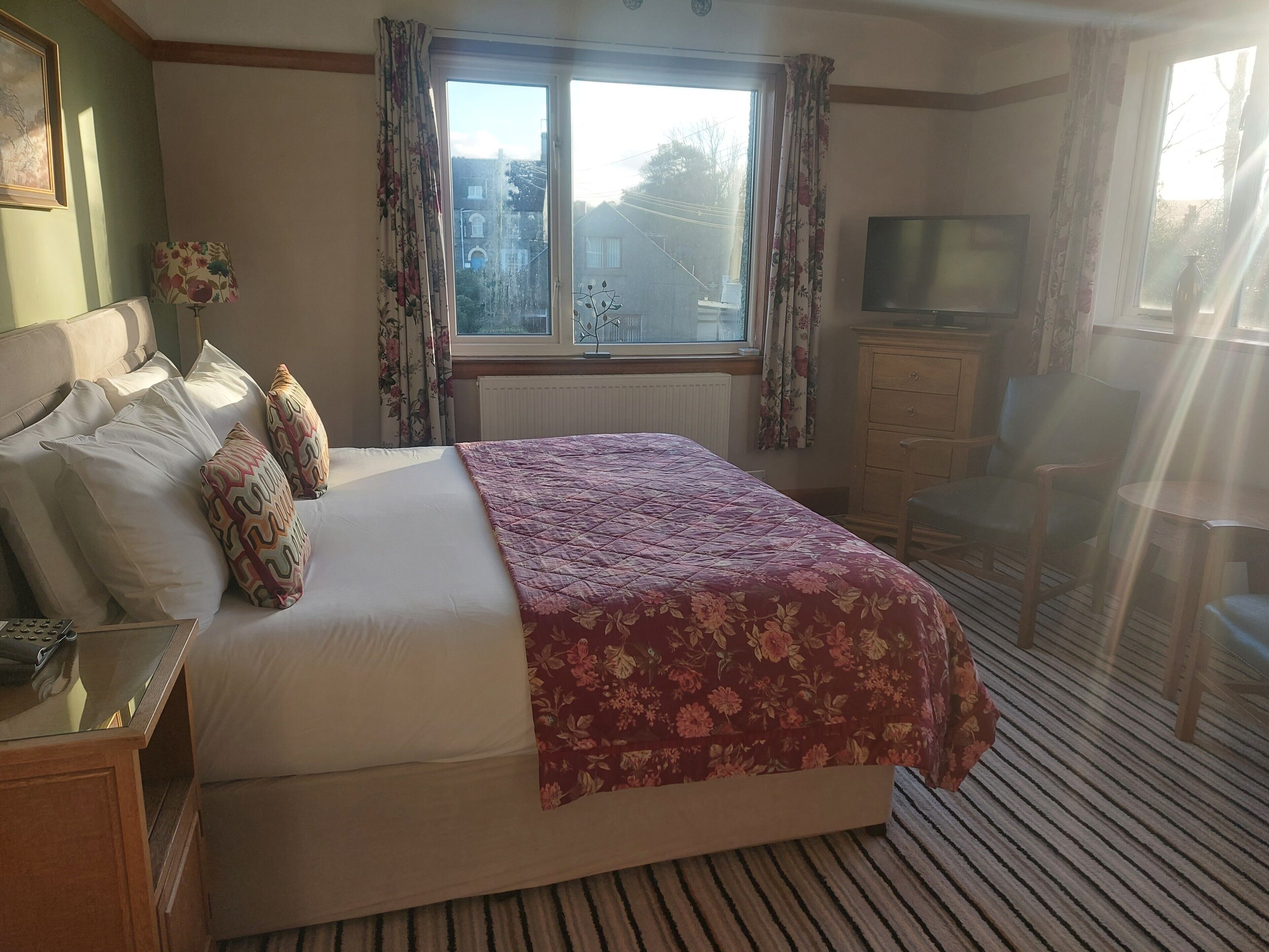 Ein Schlafzimmer mit Bett, Fernseher, einem Holzschrank und einem Fenster mit Vorhängen.