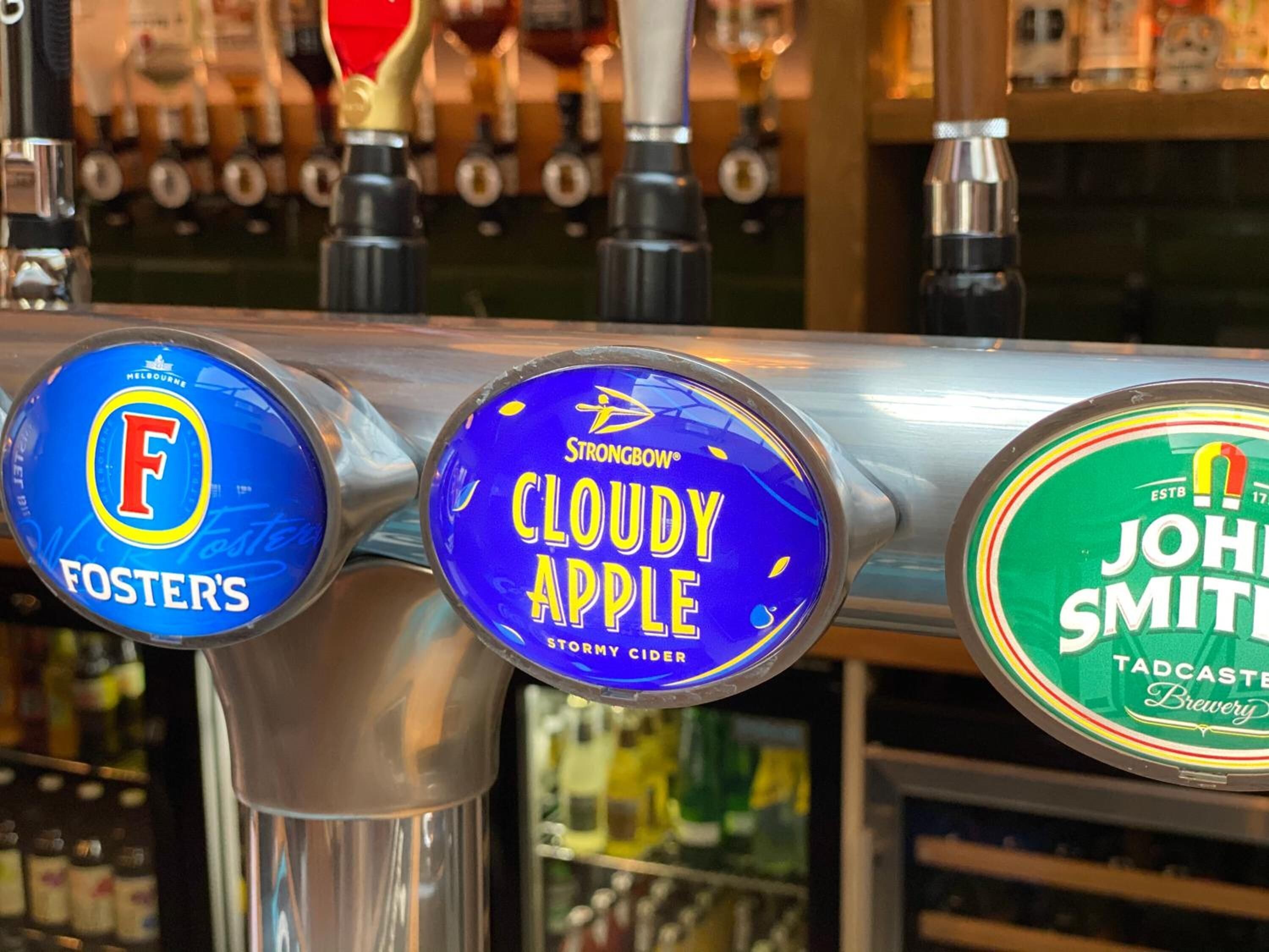 A bar with three taps labeled 'Foster's', 'Strongbow Cloudy Apple', and 'John Smith'.