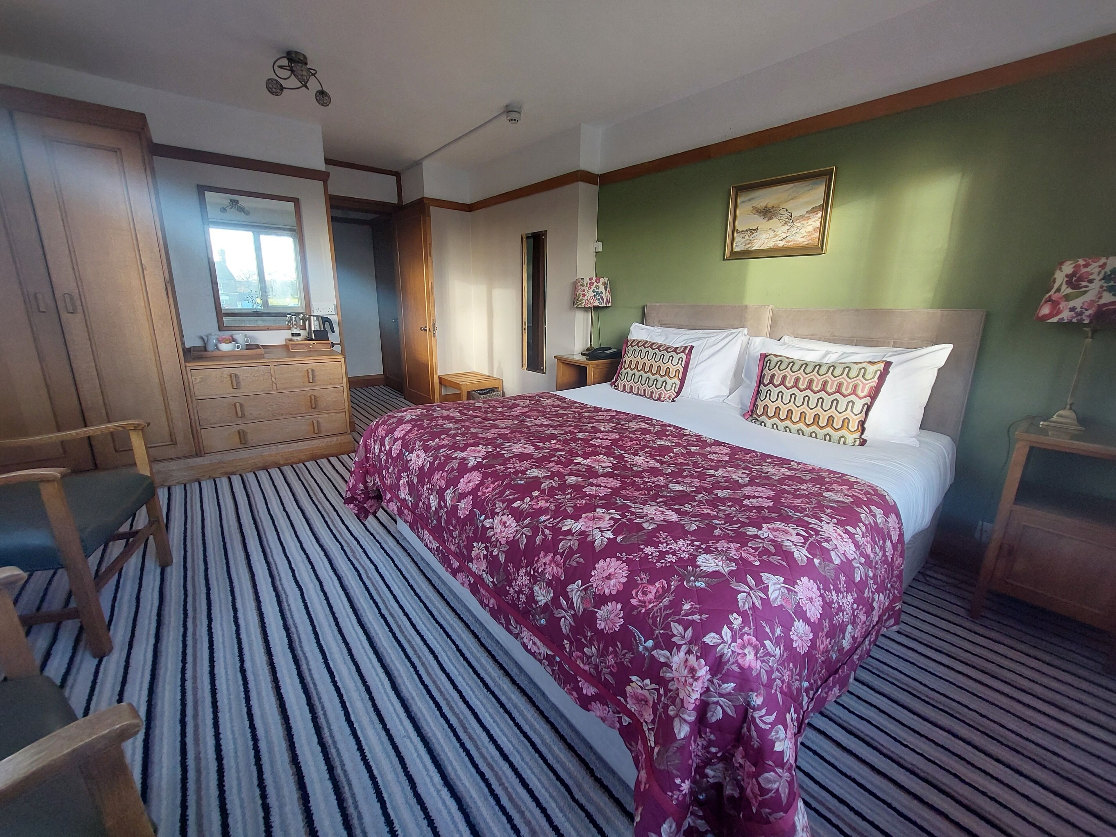 Un dormitorio con una cama grande, un aparador de madera, un espejo y una pared de acento verde.