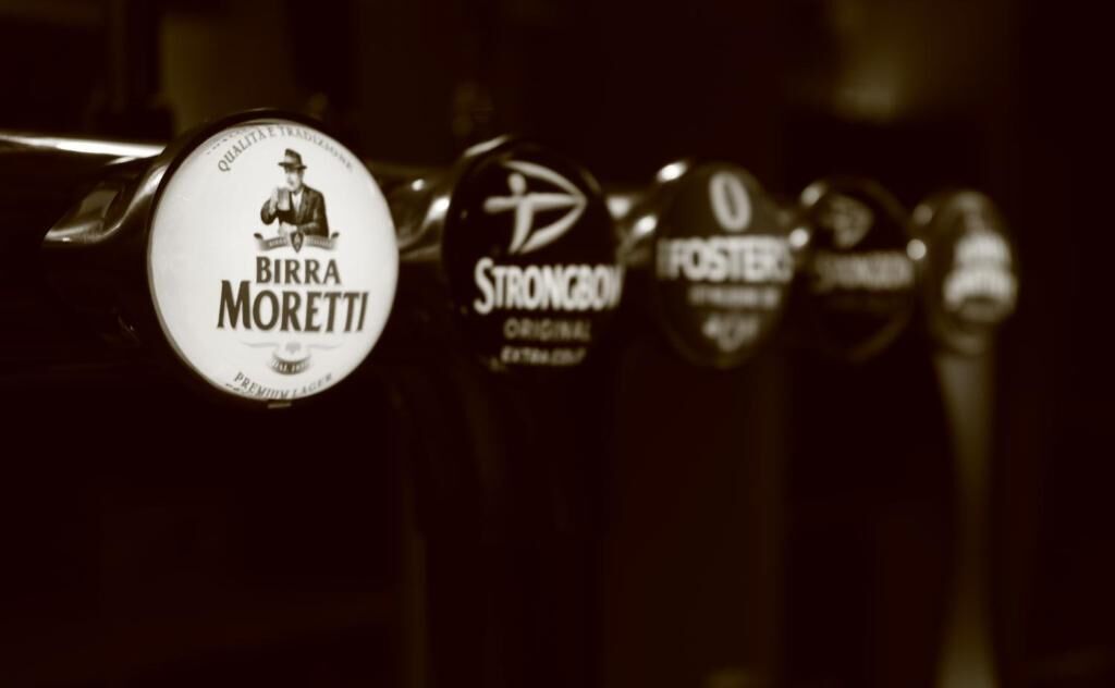 A row of beer bottles with labels, including brands like Birra Moretti and Strongbow.