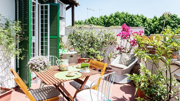 A patio with a wooden table, two wicker chairs, and potted plants. - Otranto - WR Apartments (Rome)