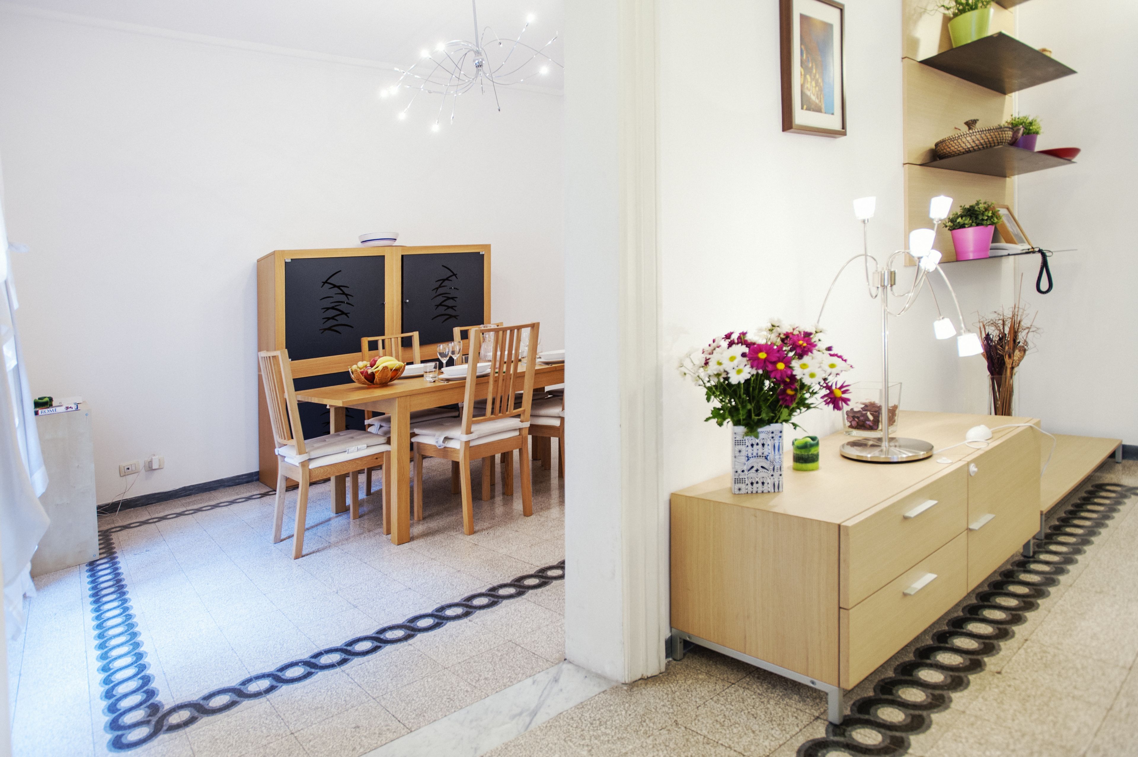 Un comedor con una mesa y sillas de madera, un florero con flores y una lámpara moderna.