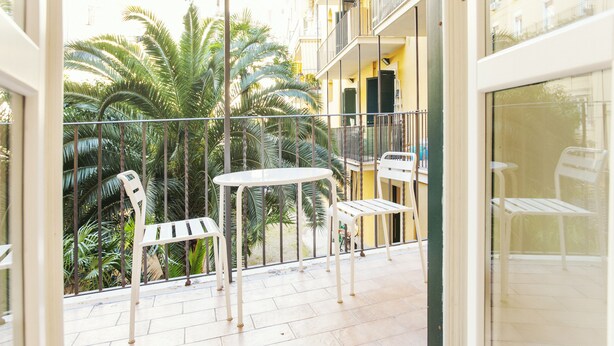 A balcony with a white table and two white chairs, overlooking a garden with palm trees. - Palestrina - WR Apartments (Rome)