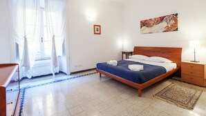 A hotel room with a bed, a nightstand, a lamp, a painting on the wall, and a window with sheer curtains. - Palestrina - WR Apartments (Rome)
