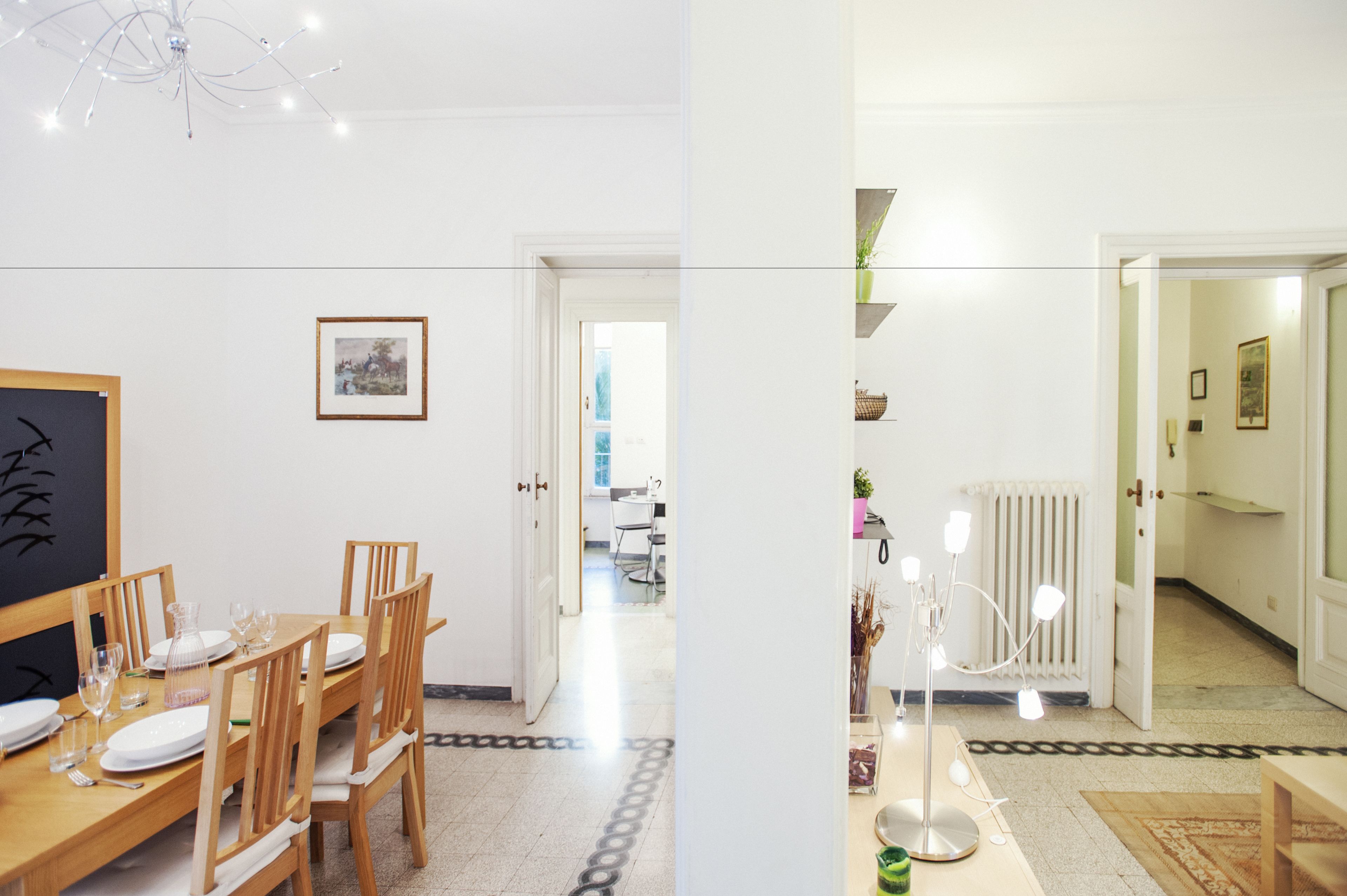 A dining area with a wooden table set for four, a framed picture on the wall, and a chandelier.