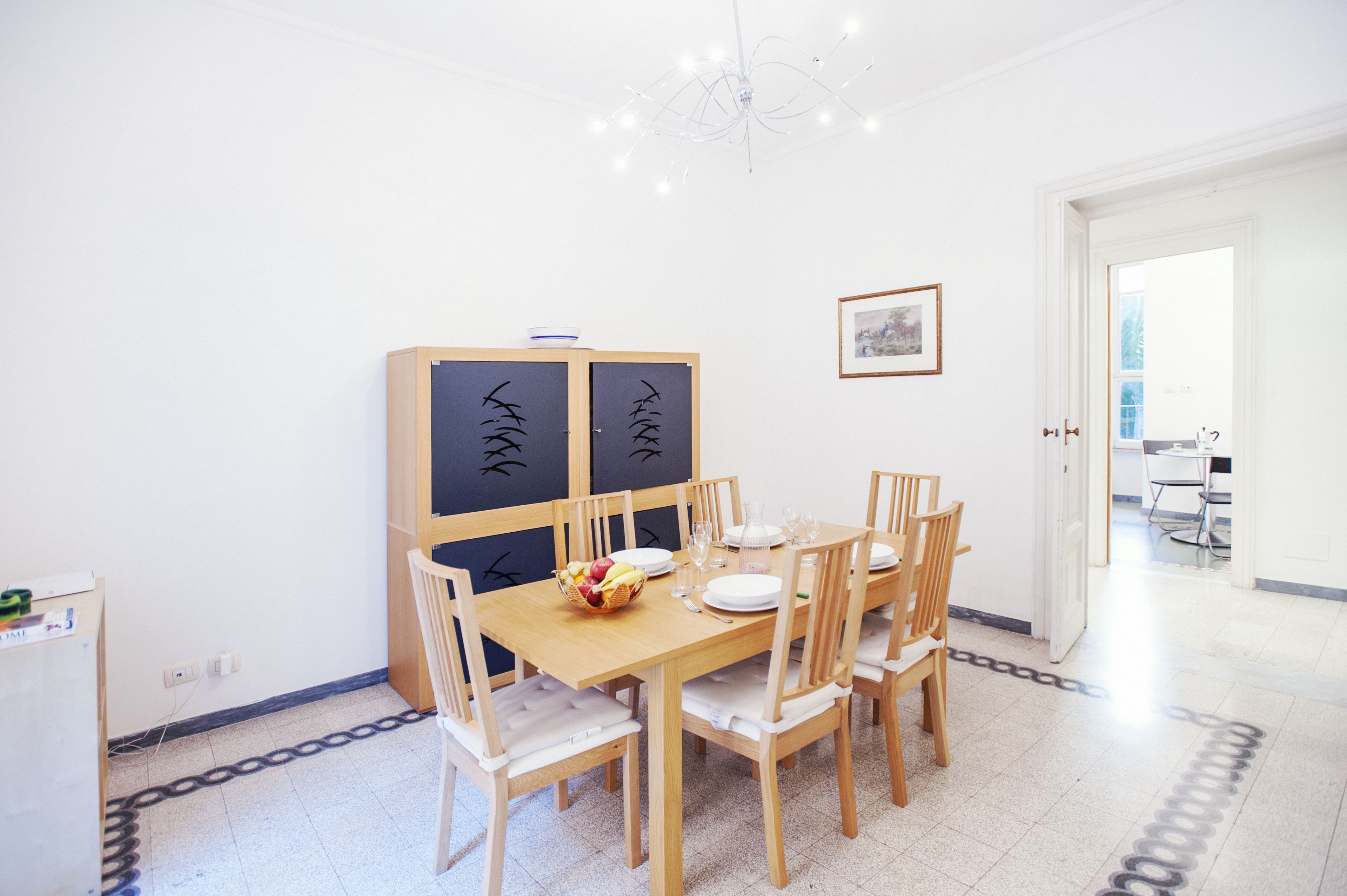 A dining area with a wooden table set for four, surrounded by chairs. There is a decorative cabinet with black designs on the wall behind the table.