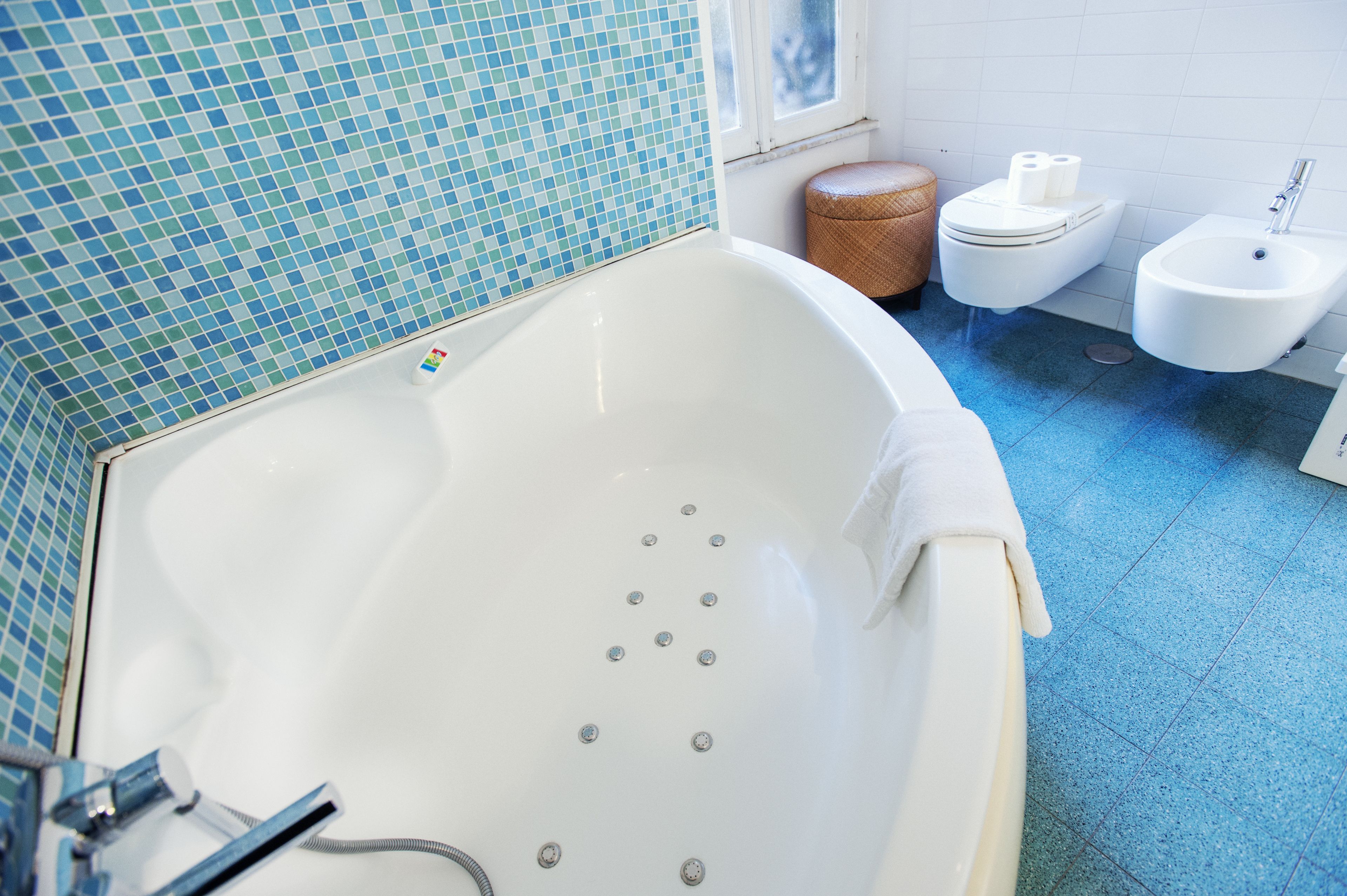 Et badeværelse med et stort badekar, toilet, bidet og en lille fletstol.