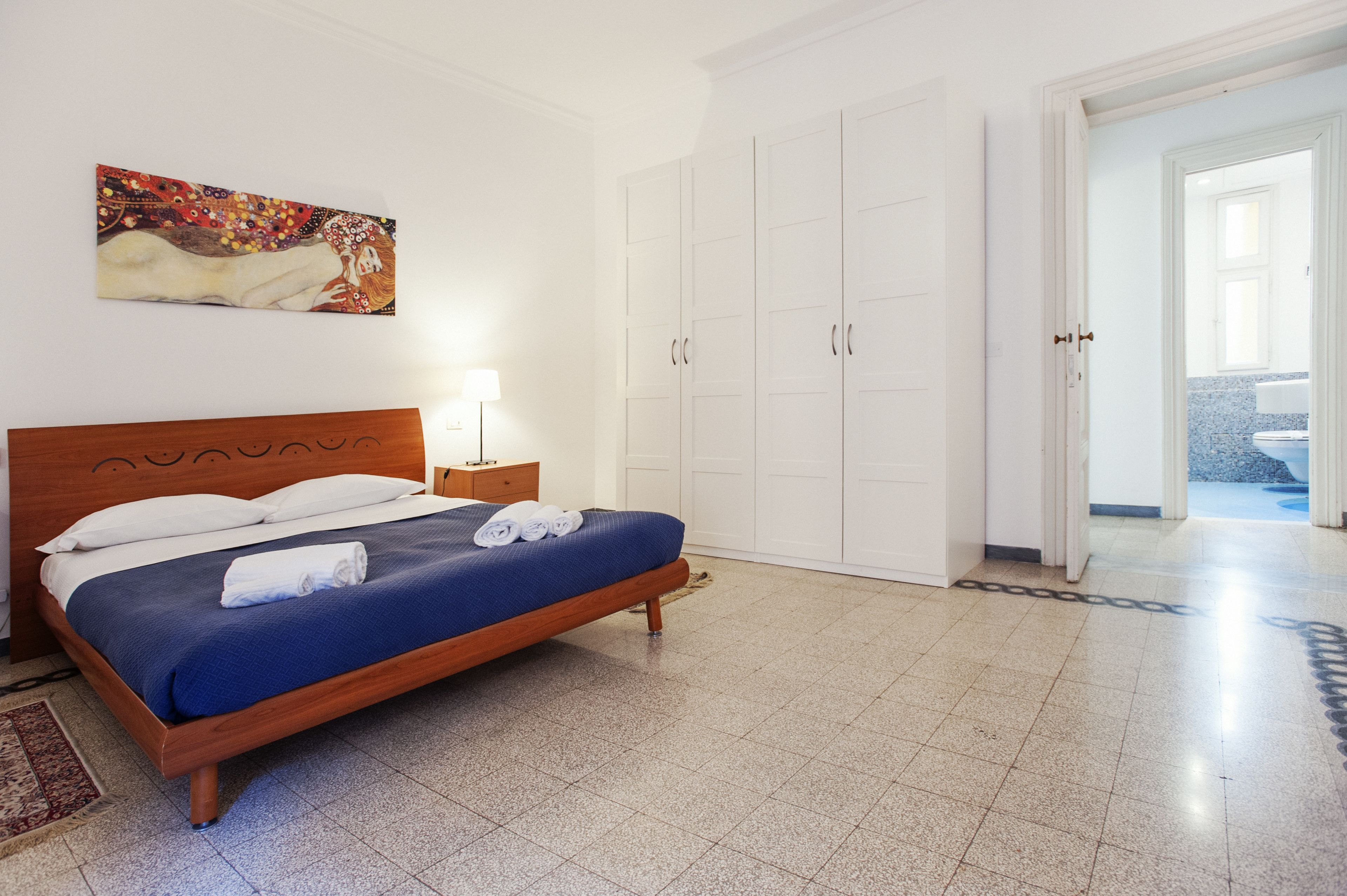 A hotel room with a bed, a nightstand, a painting on the wall, and a wardrobe.