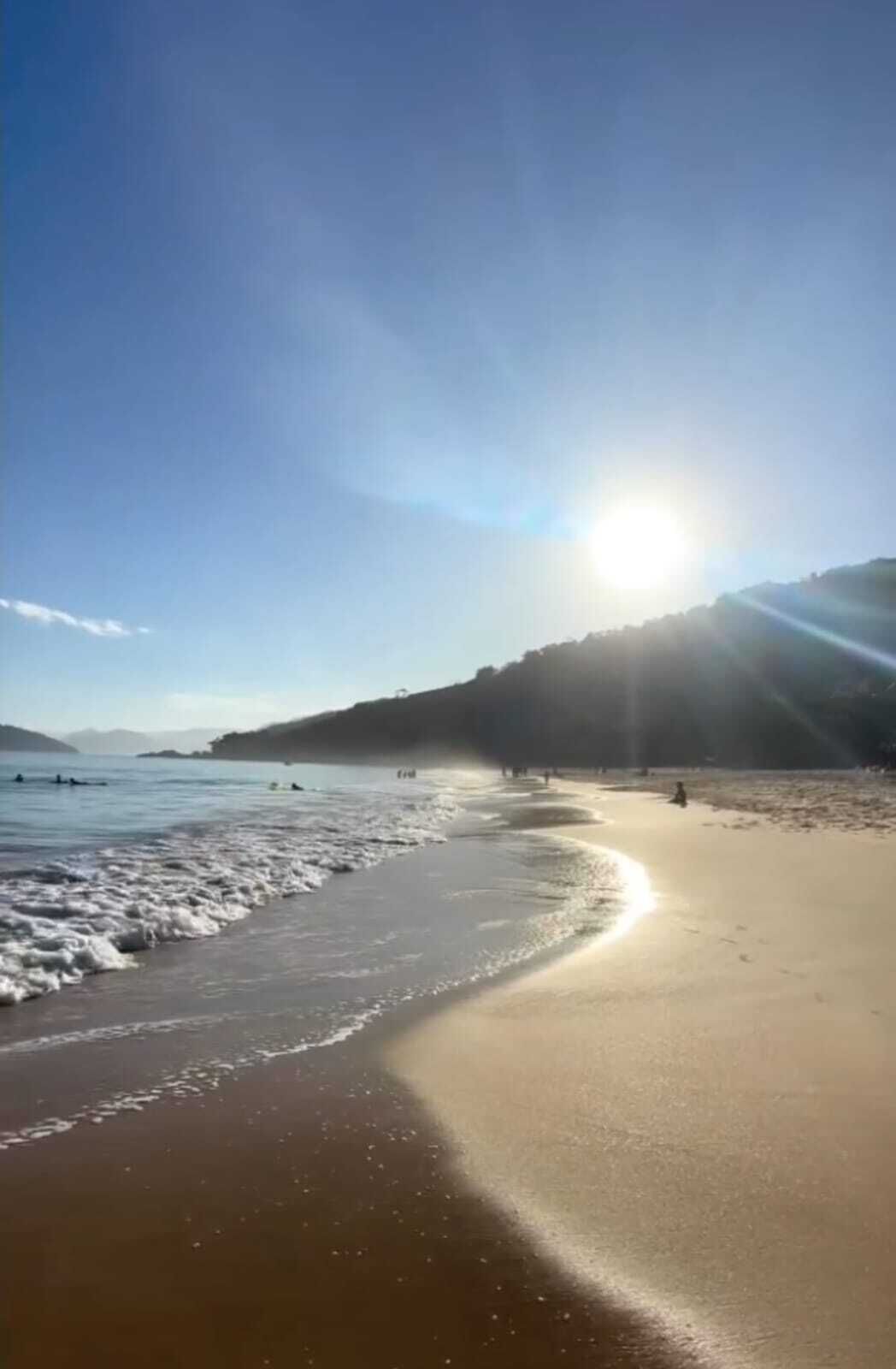 A beach with a clear sky and sunlight reflecting on the water.