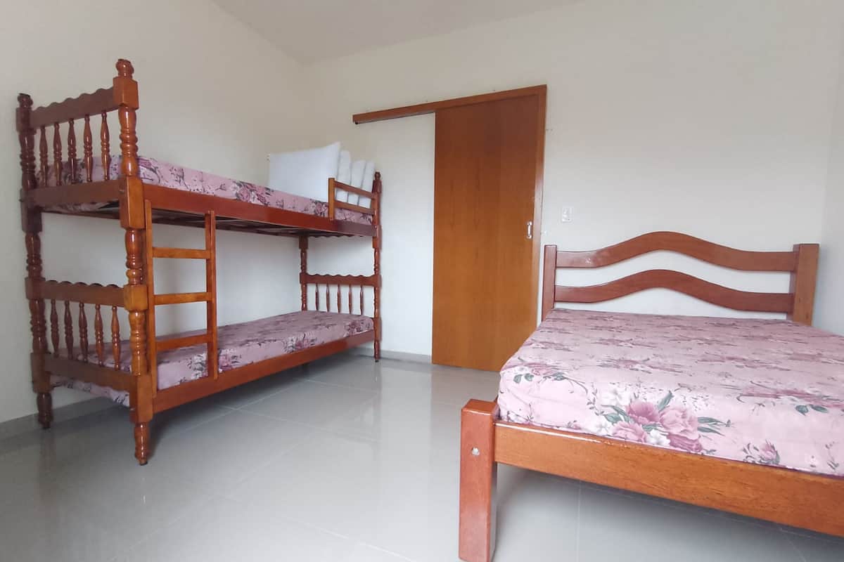 Quarto com uma cama de solteiro e uma beliche, ambos com roupa de cama florida.