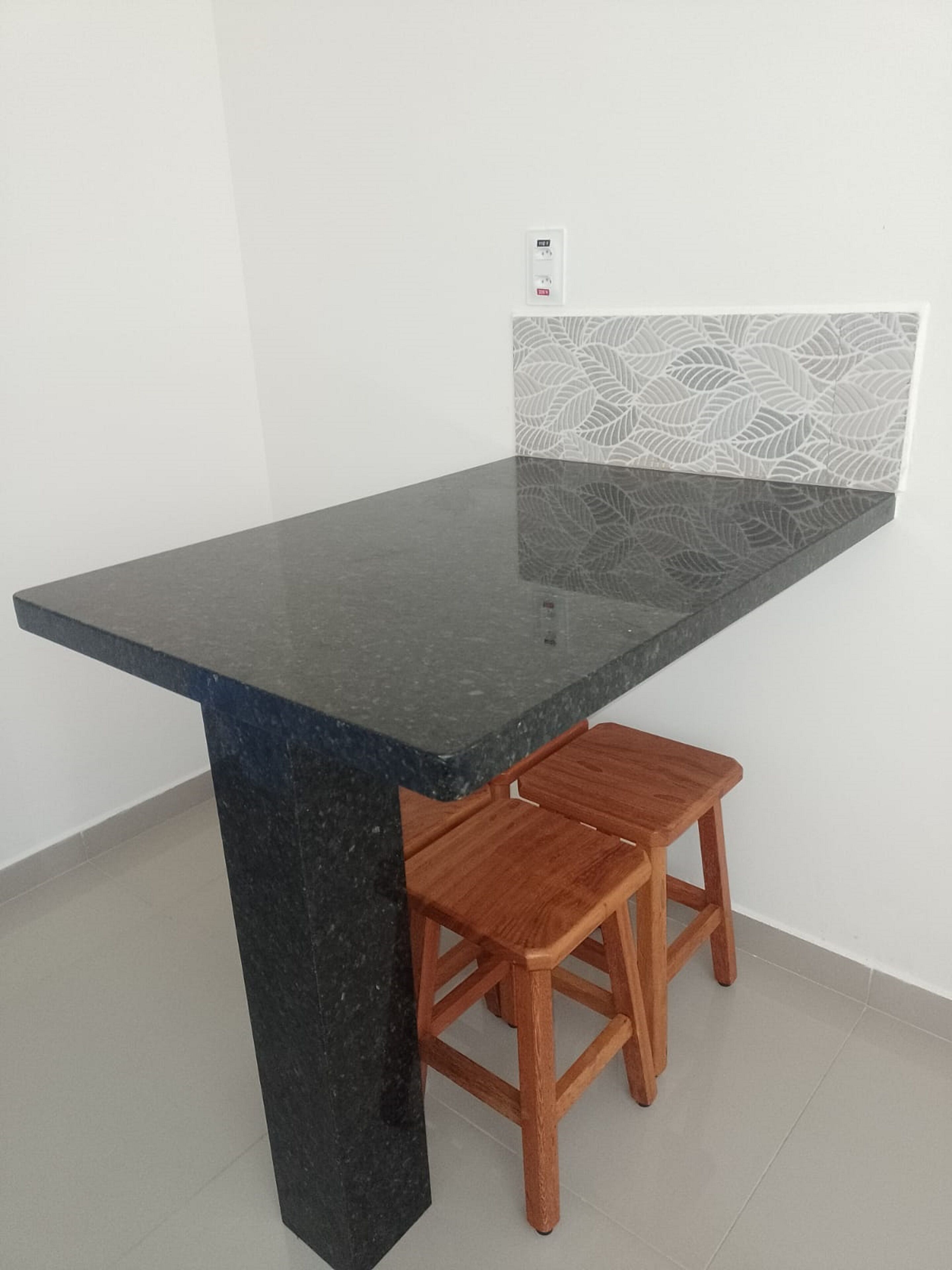 Une cuisine dotée d’un plan de travail en granit foncé, de tabourets en bois et d’un crédence blanc.