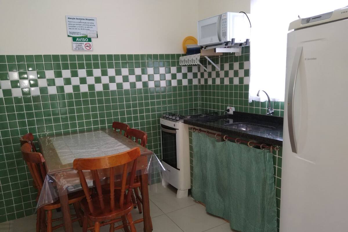 Cozinha com painel de azulejos, micro-ondas, fogão e mesa de jantar com cadeiras.