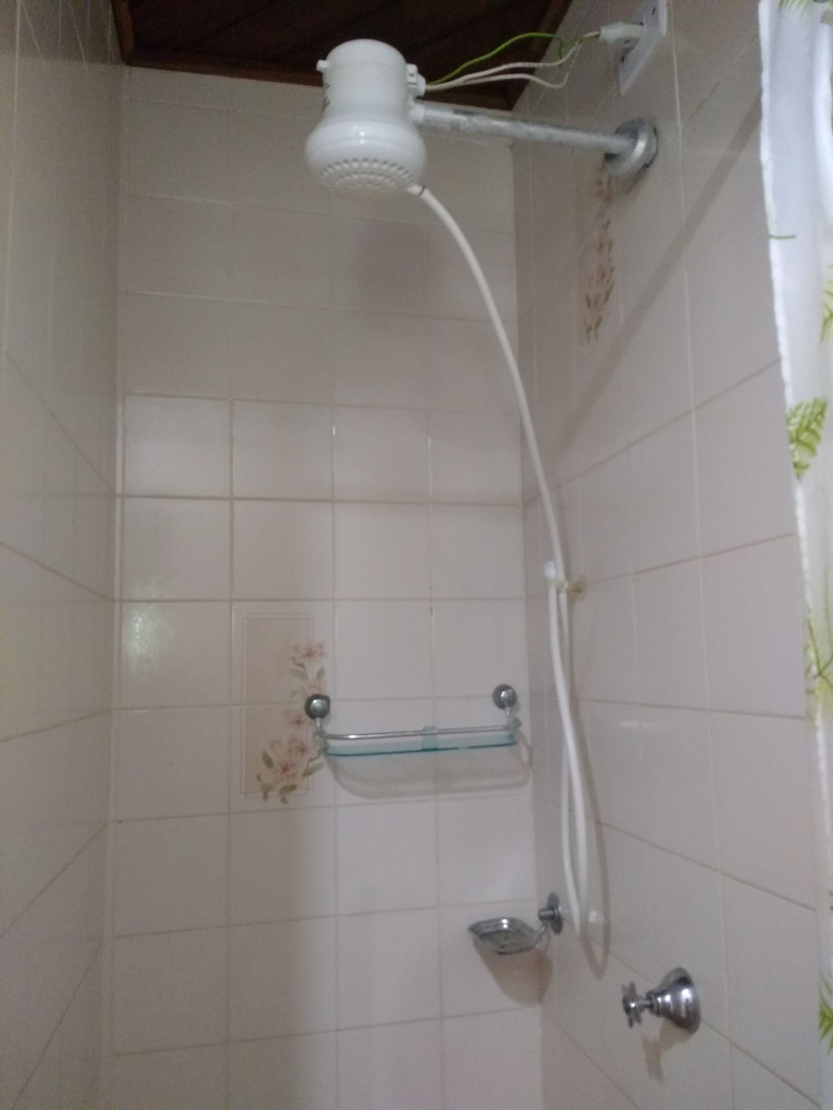 Ducha con cabezal de ducha de mano, repisa de vidrio y grifo empotrado en la pared.