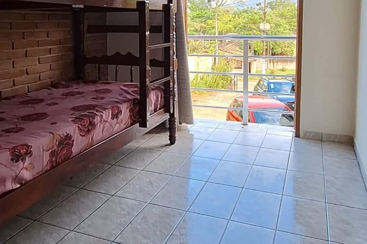 Quarto com beliche, ventilador e vista para um estacionamento e área verde lá fora.