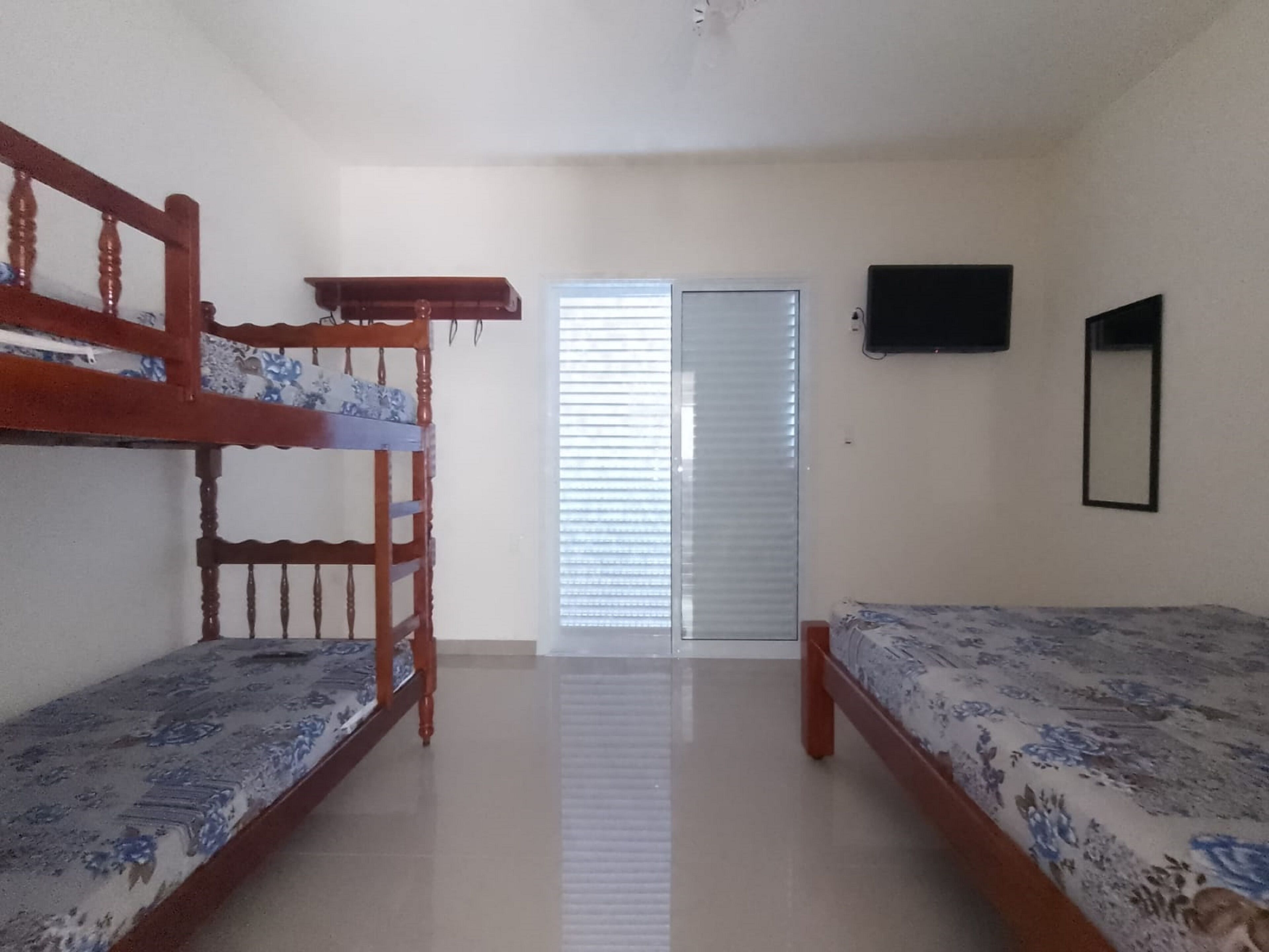 A room with two bunk beds, a flat-screen TV mounted on the wall, and a door with blinds.