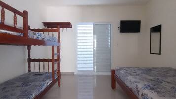 A room with two bunk beds, a flat-screen TV mounted on the wall, and a door with blinds.