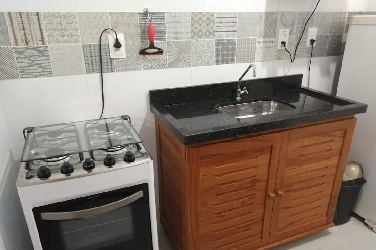 Cozinha com fogão a gás, forno, armários de madeira e bancada preta.
