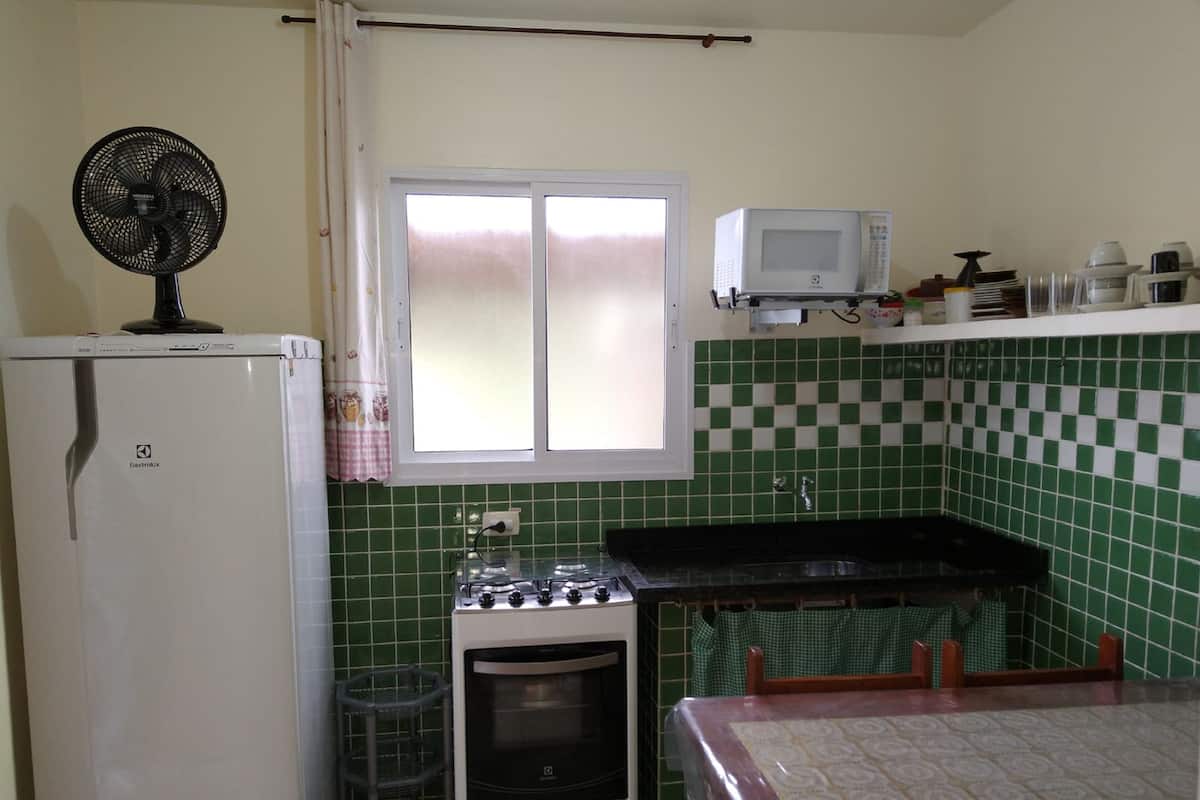 Uma cozinha compacta com geladeira, fogão, micro-ondas e uma janela com cortinas.