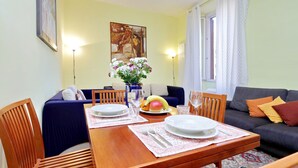 A dining area with a wooden table set for two, a sofa, and a painting on the wall. - Romalibera - WR Apartments (Rome)