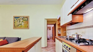 A kitchen with a wooden countertop, a stove, and a sink. There is a painting on the wall and a hallway leading to another room. - Romalibera - WR Apartments (Rome)