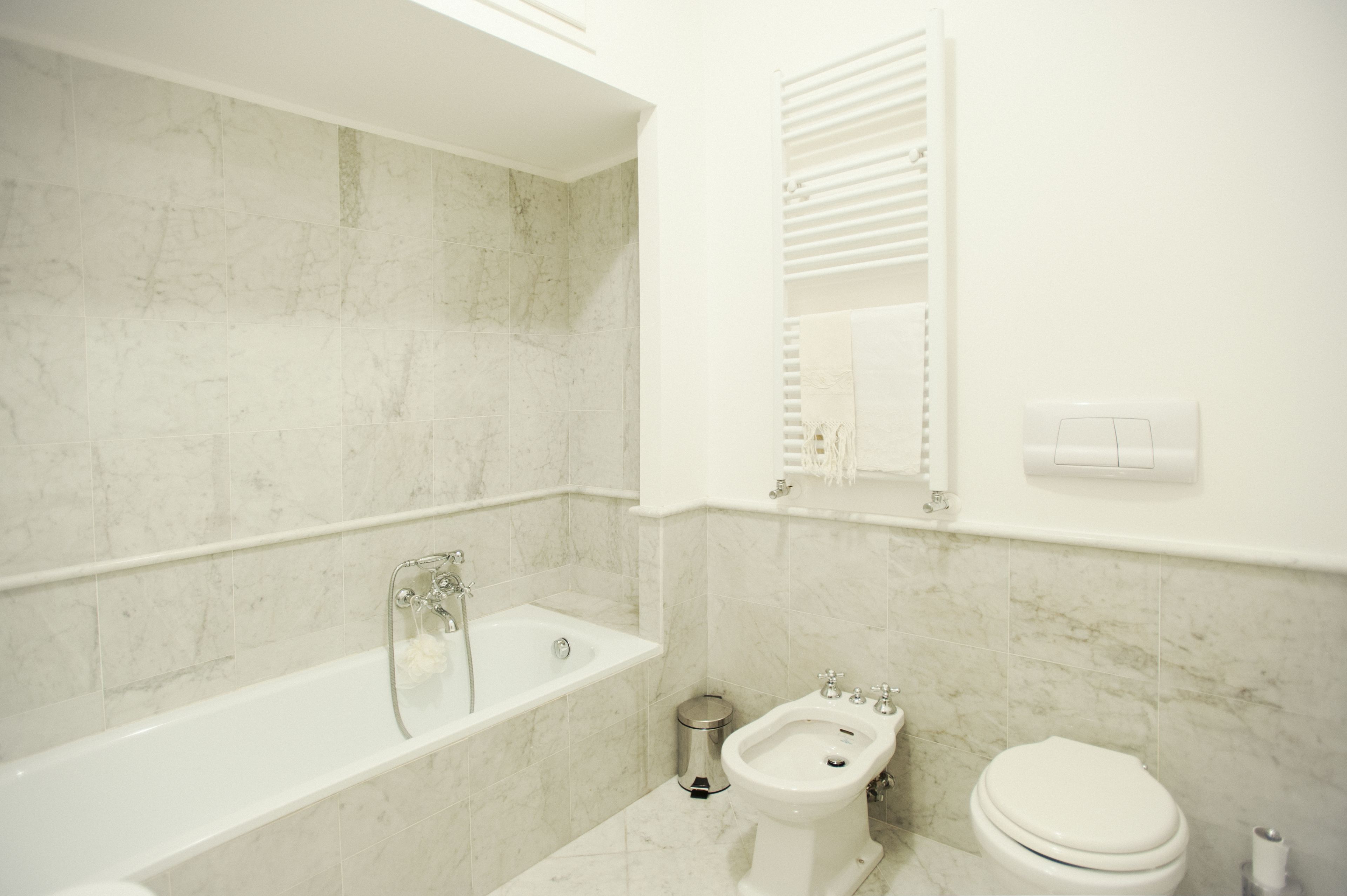 A bathroom with a bathtub, bidet, toilet, and a mirror with a towel rack.